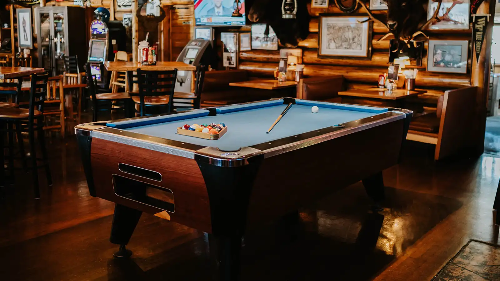 A pool cue and pool balls sit on top of the pool table surrounded by tables and booths inside the Corral Bar and Steakhouse.